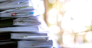 A stack of papers held together by binder clips and paper clips in front of a blurred out background.