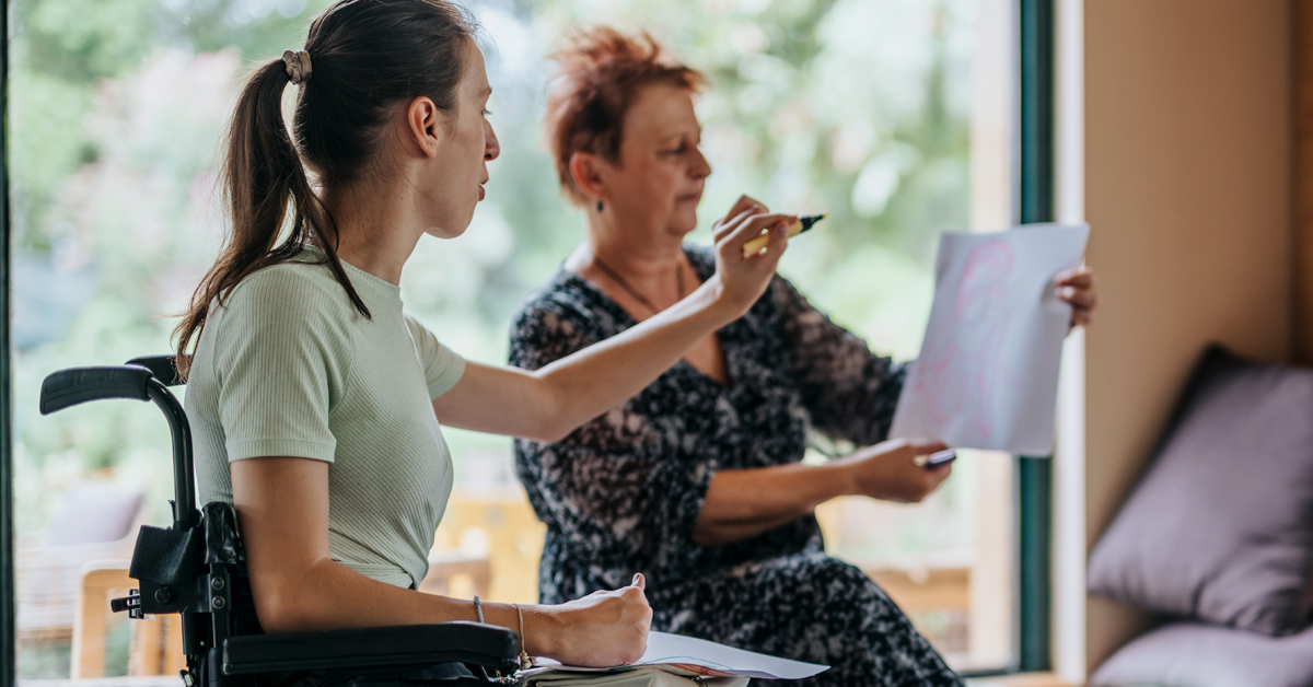 A group of diverse individuals, including someone in a wheelchair, engaged in a collaborative meeting in a cozy room setting. They are actively sharing and discussing ideas.