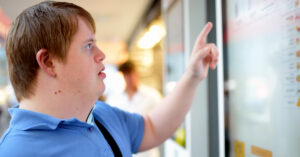 A white man with Down syndrome points at a digital menu board