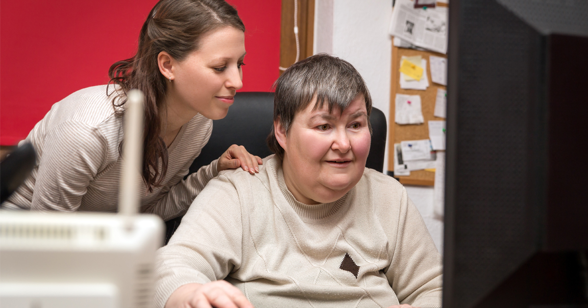 Two women, one who has a disability, look at a computer in an office setting